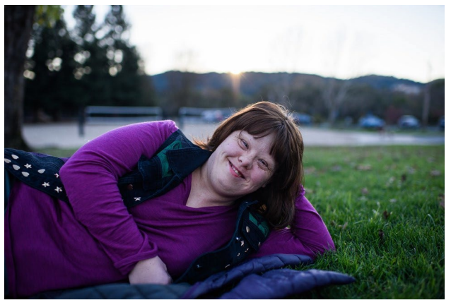 A young woman with down syndrome lying on her side, smiling, holding her head up with her hand.
