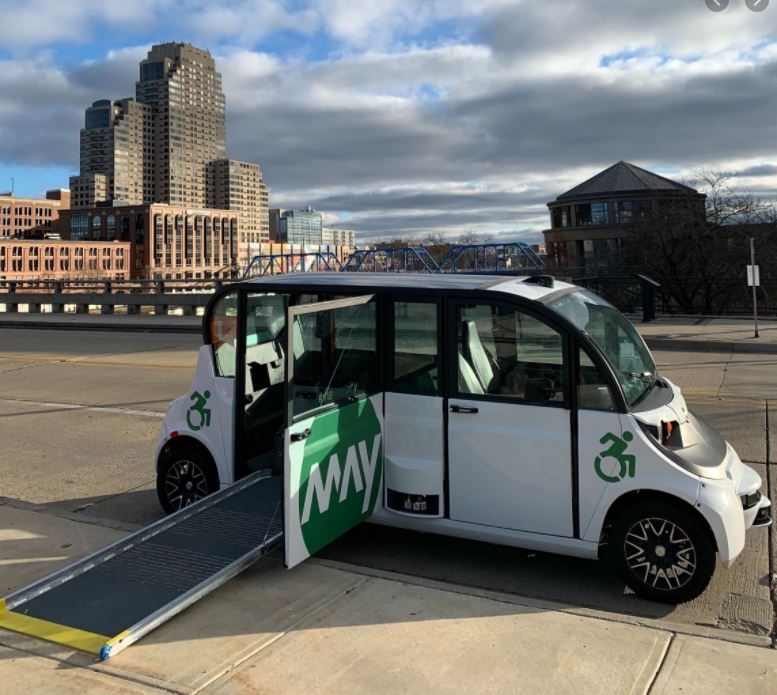 Accessible May Mobility Shuttle in in Grand Rapids, Michigan. White shuttle van with a door open and a wheelchair ramp extended out.