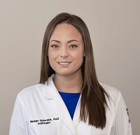 A white woman smiling, with long brown hair, wearing a blue shirt underneath a white lab coat.