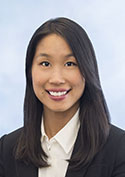 An woman of Asian descent smiling, wearing a white blouse with a black coat. She has long black hair.