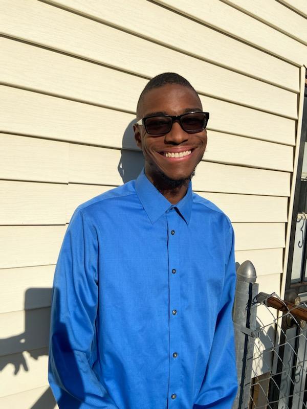 Picture of Marcellus Castleberry. He is smiling and leaning against a building. He has black hair and is wearing a blue shirt.