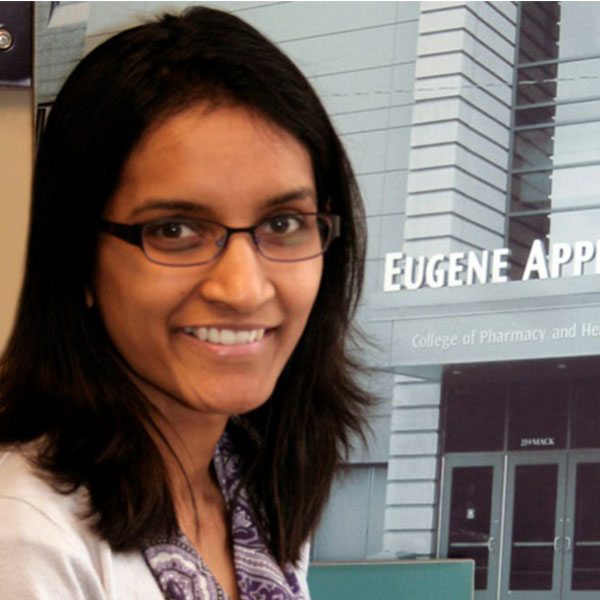 A picture of Preethy Samuel. Preethy has shoulder-length black hair and is wearing a purple patterned blouse, white coat, and black glasses.
