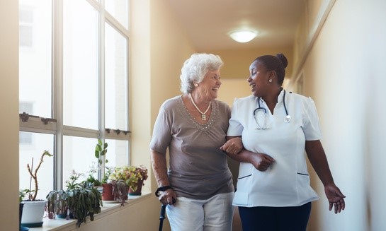 A woman with white hair is walking with a arm-in-arm with a healthcare provider.